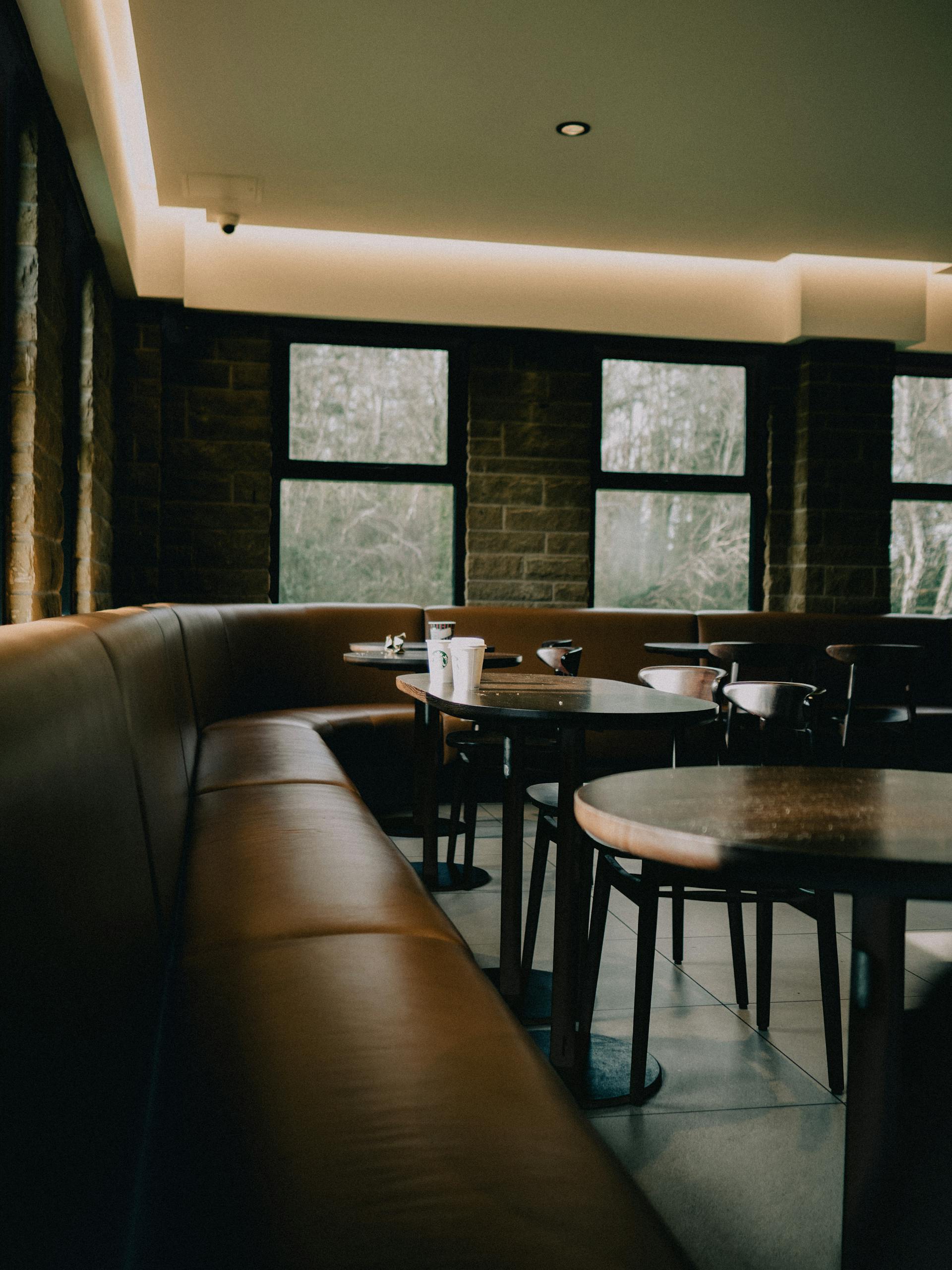 Salle du bistrot avec banquettes cuir cognac, tables rondes, lumière naturelle